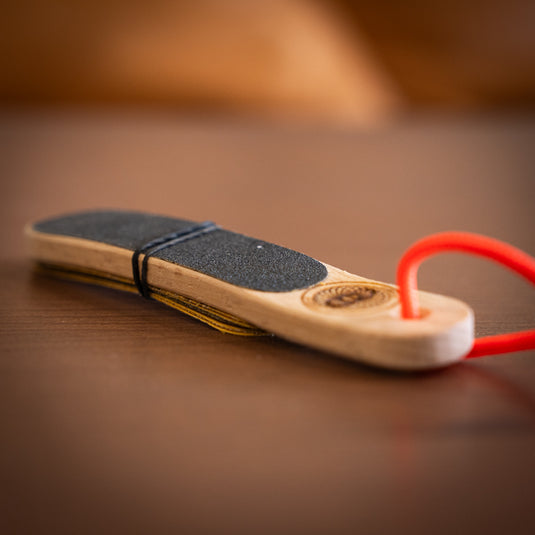 Wooden hand file with black paper, orange cord loop. Laid on wooden surface.