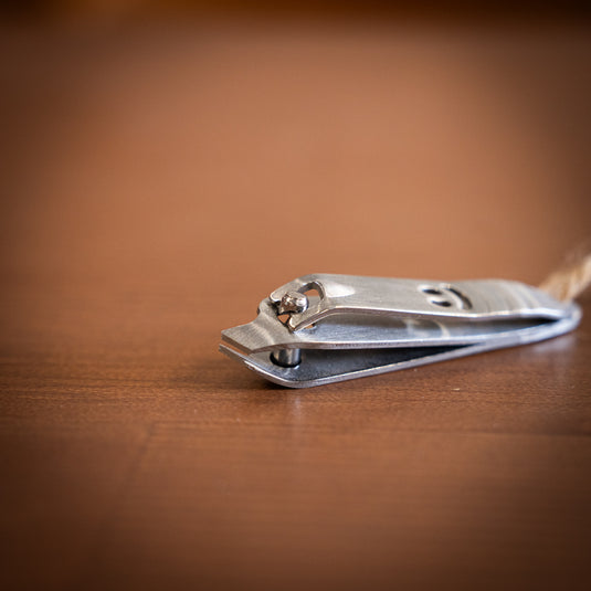 Close-up of a stainless steel nail clipper with a smiling face design, resting on a wooden surface.