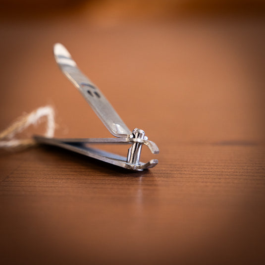 Close-up of a stainless steel nail clipper with a smiling face design in "open" postition, resting on a wooden surface.