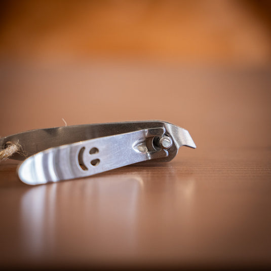 Close-up of a stainless steel nail clipper with a smiling face design, resting on a wooden surface.