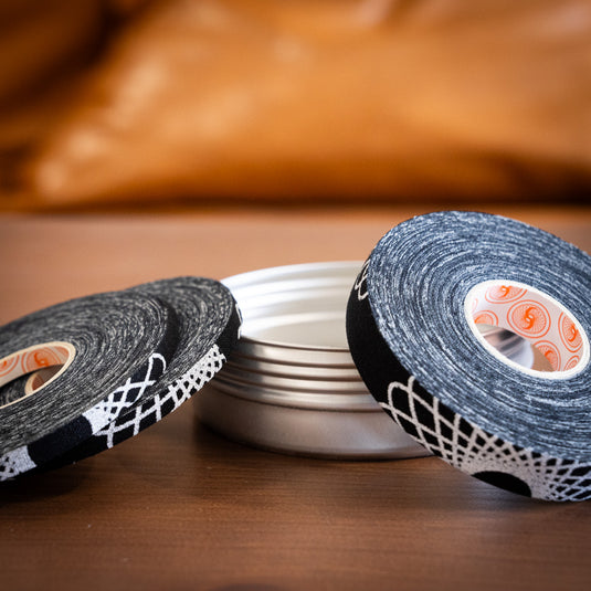 Three rolls of ClimbSkin Tape of varied thickness in black with white spiral design. Laid on top of one another on wooden surface.