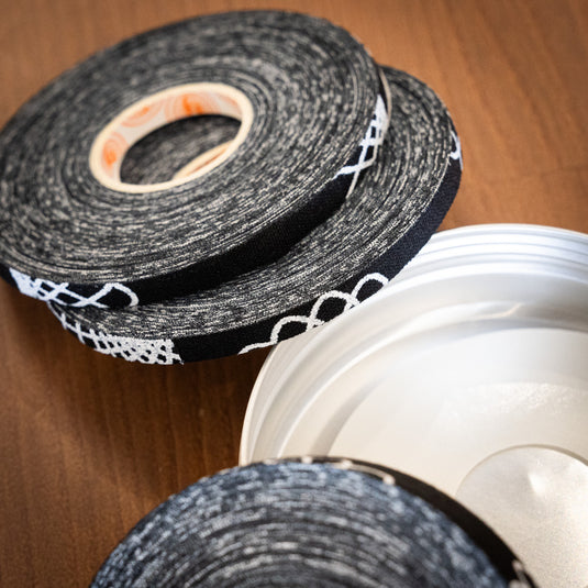 Three rolls of ClimbSkin Tape of varied thickness in black with white spiral design. Laid on top of one another on wooden surface.
