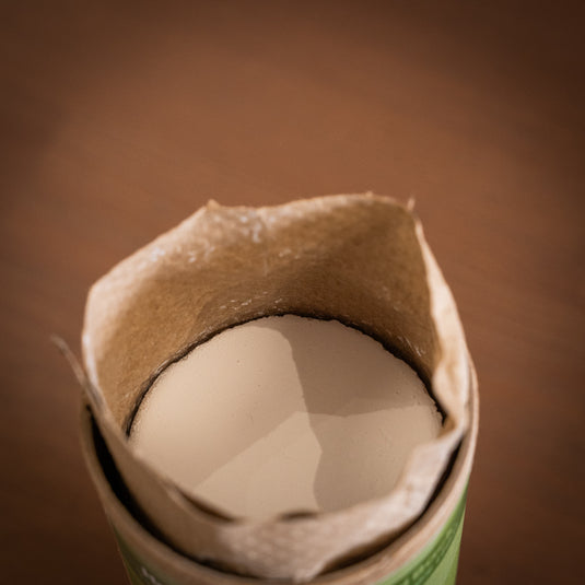 A close up image of an open container of Friction Labs Premium Chalk Discs displaying the paper packaging coming out the top and a disc of compacted chalk.