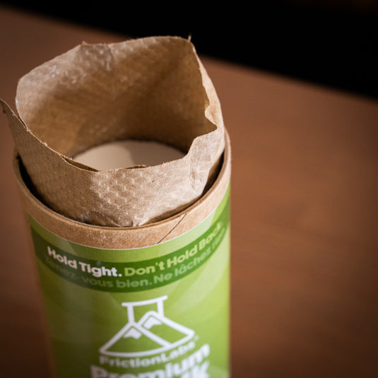 An opened cylindrical container of Friction Labs Premium Chalk Discs displaying the recyclable paper packaging coming out the top of the container.