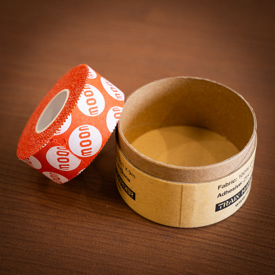 A roll of bright orange fabric tape with repeating "moon" design sits next to cardboard packaging on a wooden surface.