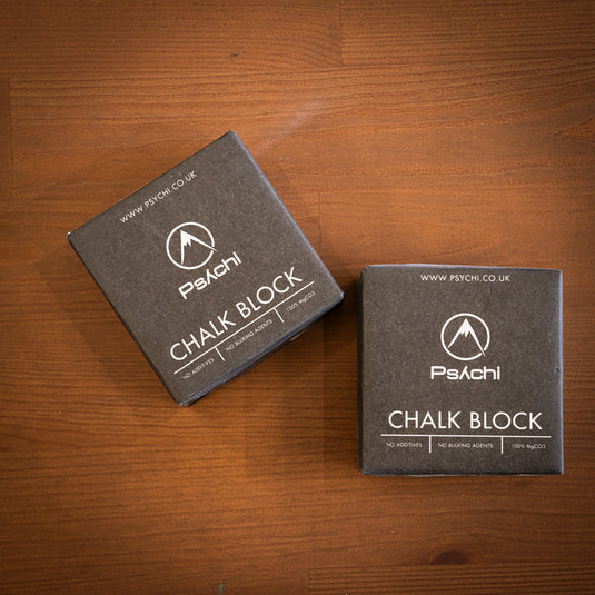 Two blocks of Psychi Chalk in black square paper packaging, displayed laydown on a wooden surface.