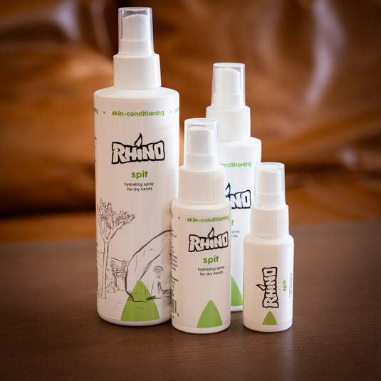 Four spray bottles of Rhino Spit - hydrating spray for dry hands of varying sizes. Displayed on wooden surface.