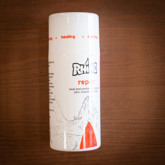 Large pump bottle of Rhino Skin Repair - heal and soothe sore and worn skin. In red and white design laid on wooden surface.