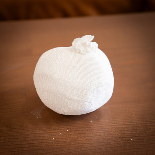 Ball of Chalk in white netting material. Displayed on wooden surface with a few specs of chalk on the surface.