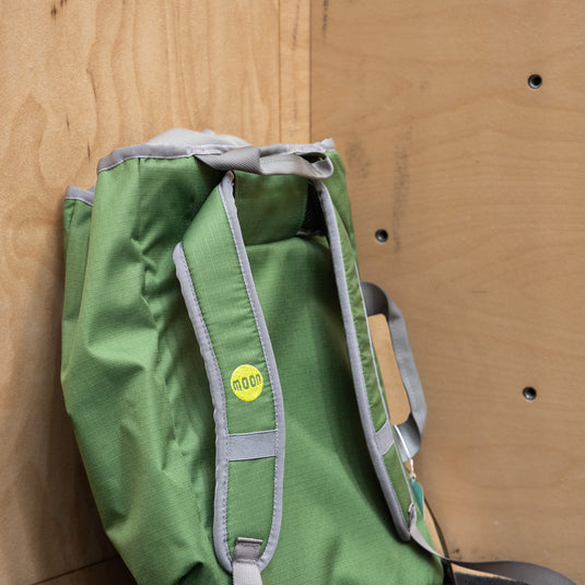 Moon Bouldering Bag - Green in backpack style showing back straps laid against wooden surface