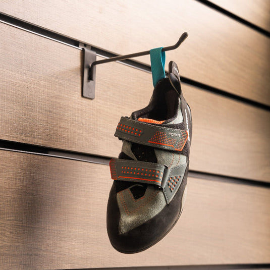 A climbing shoe, Scarpa Force Womens, hanging on a black hook against a textured metallic background.