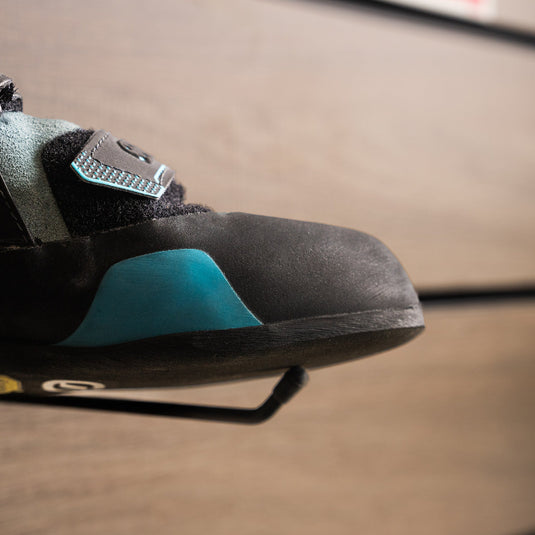 A close up Scarpa Force toe box, resting on black wall hook against metallic background.