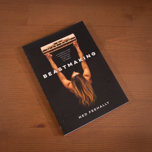 Beastmaking - a fingers first approach to becoming a better climber. Features athlete shauna coxey hanging on a beastmaker 2000 on the cover laid on wooden surface