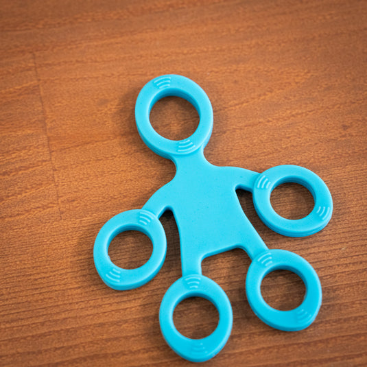 Blue finger trainer shaped like five inter-connected circles, resting on wooden surface.