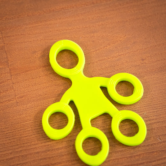 Green finger trainer shaped like five inter-connected circles, resting on wooden surface.