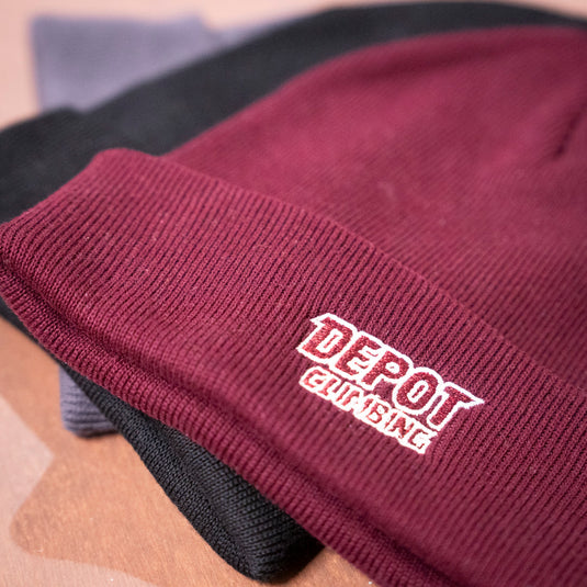 Depot Beanie in various colours laid on wooden surface