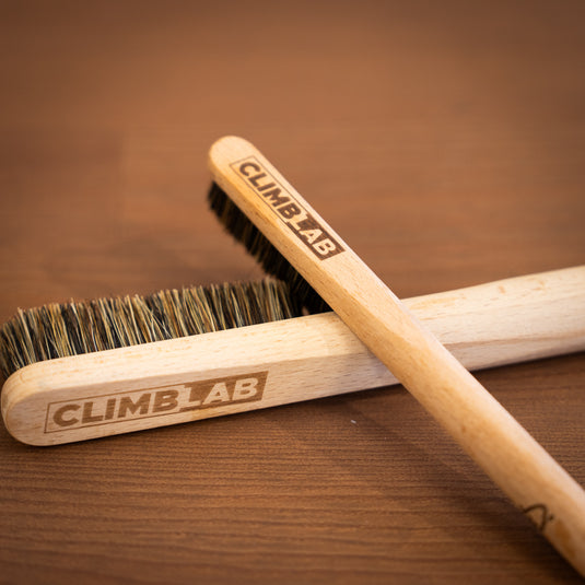 Two wooden climbing brushes with "CLIMBLAB" engraved, resting on a wooden surface, showcasing the bristle details.