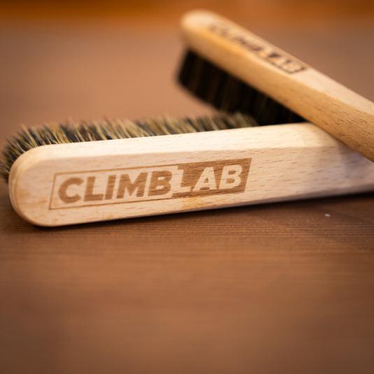 Two wooden climbing brushes with "CLIMBLAB" engraved, resting on a wooden surface, showcasing the bristle details.