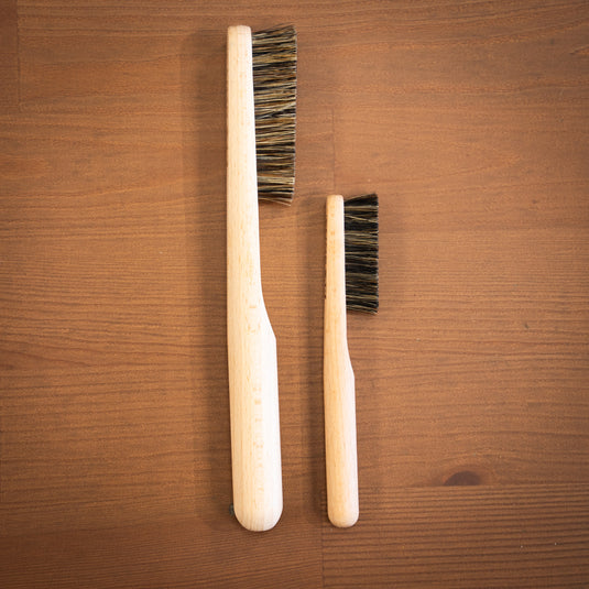 Two wooden Climb Lab brushes resting on a wooden surface, showcasing the different sizes.