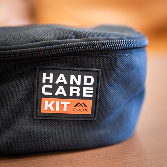 Close-up of a black hand care kit bag featuring a label that reads "HAND CARE KIT CRUX" on a wooden surface