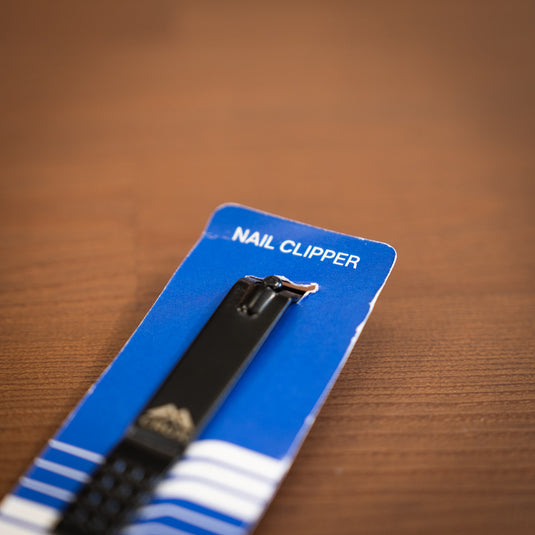 Close up of the Crux Nail Clipper in black. Displayed in blue packaging and laid on wooden surface.