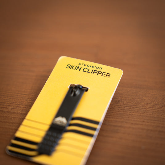 Close up of the Crux Skin Clipper in black. Displayed in yellow packaging and laid on wooden surface.