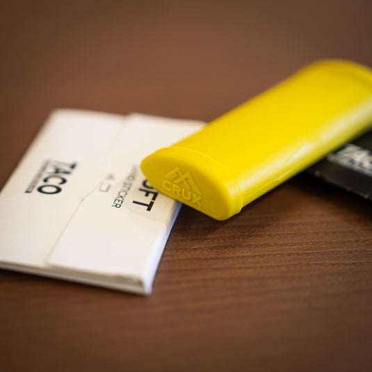 Close up of the Crux Skin File in yellow. Displayed laid down on wooden surface with replacement papers in white packet.