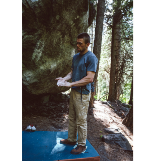 Black Diamond Ethos Pants in Khaki - Worn by climber stood on bouldering pad putting on chalk out in a wooden area next to a large boulder