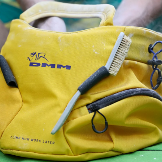 DMM Edge boulder chalk bag/bucket in yellow, with chalk brush in holder and climber chalking up
