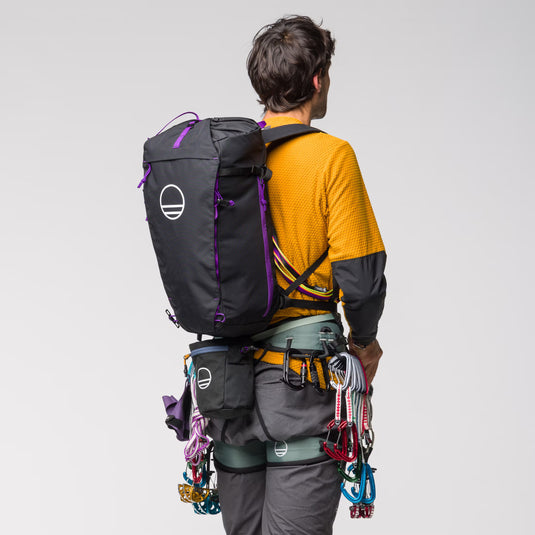 Wild Country Progress Backpack 25L - worn by model wearing harness and movement chalkbag in black with quickdraws and cams attached